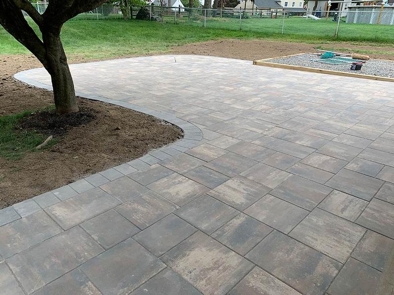a curved large paver patio with a multi-toned brown and gray surface