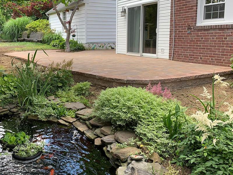 Multi-tonal hardscape paver patio built adjacent to a white and brick house